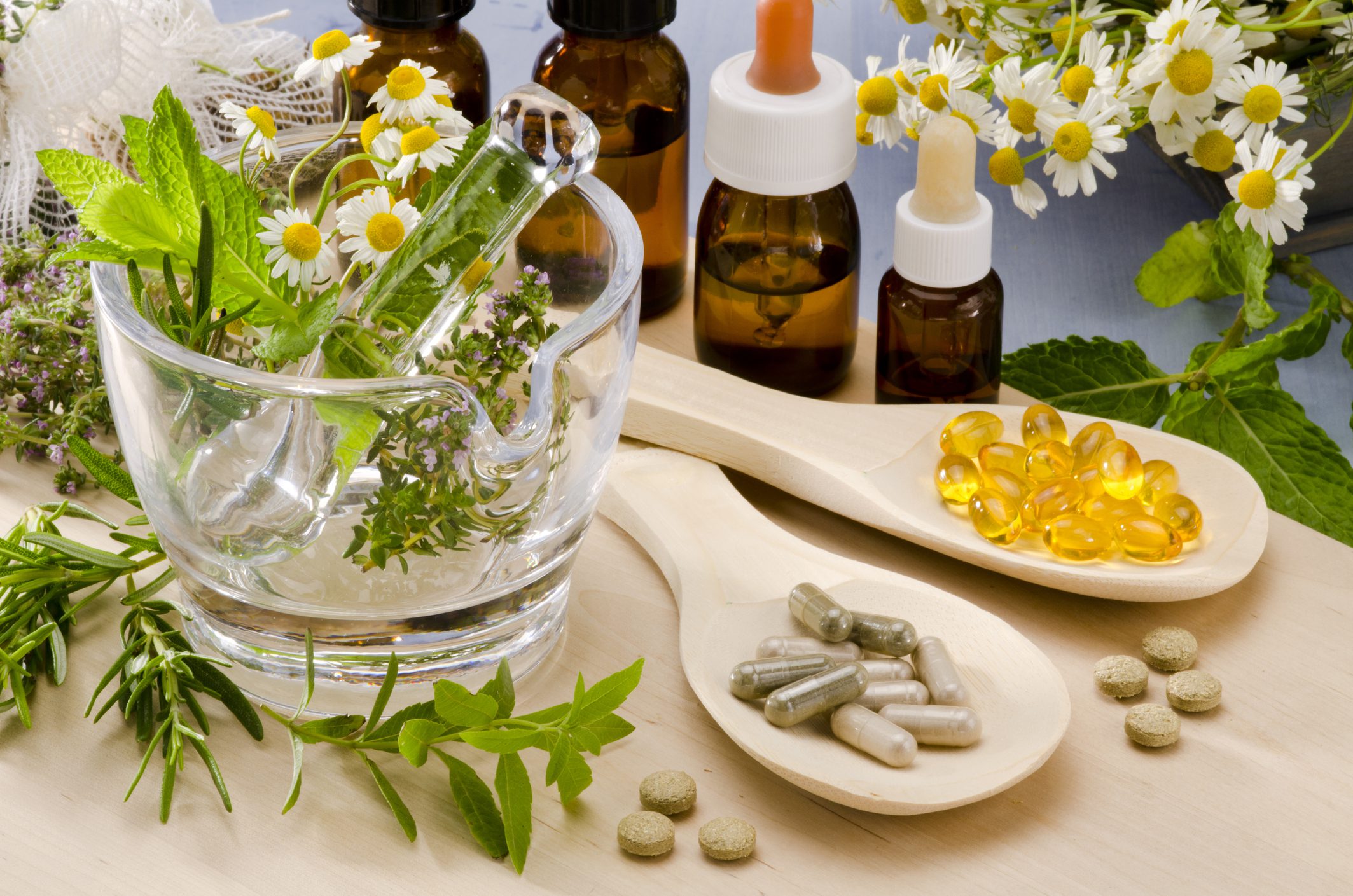 Photo of Various Herbal Remedies and Supplements on a Table With Fresh Flowers and Plants